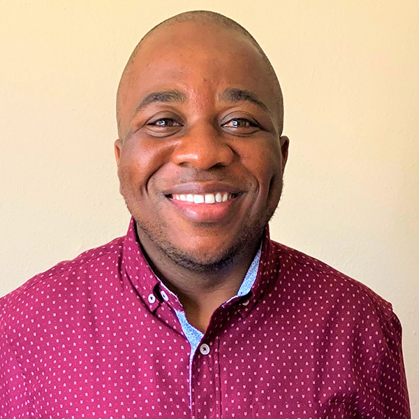 an african American man in a pink shirt smiles at the camera