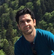 a man with dark hair and trees in the background