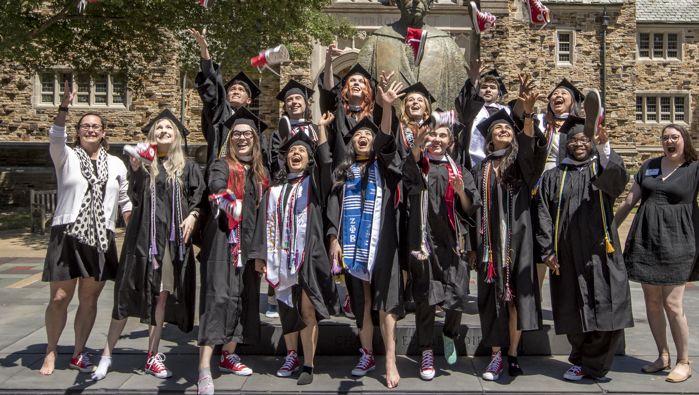 students in graduation robes toss red tennis shoes into the air