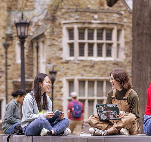 Students gather, talking, in front of a large collegiate gothic building.