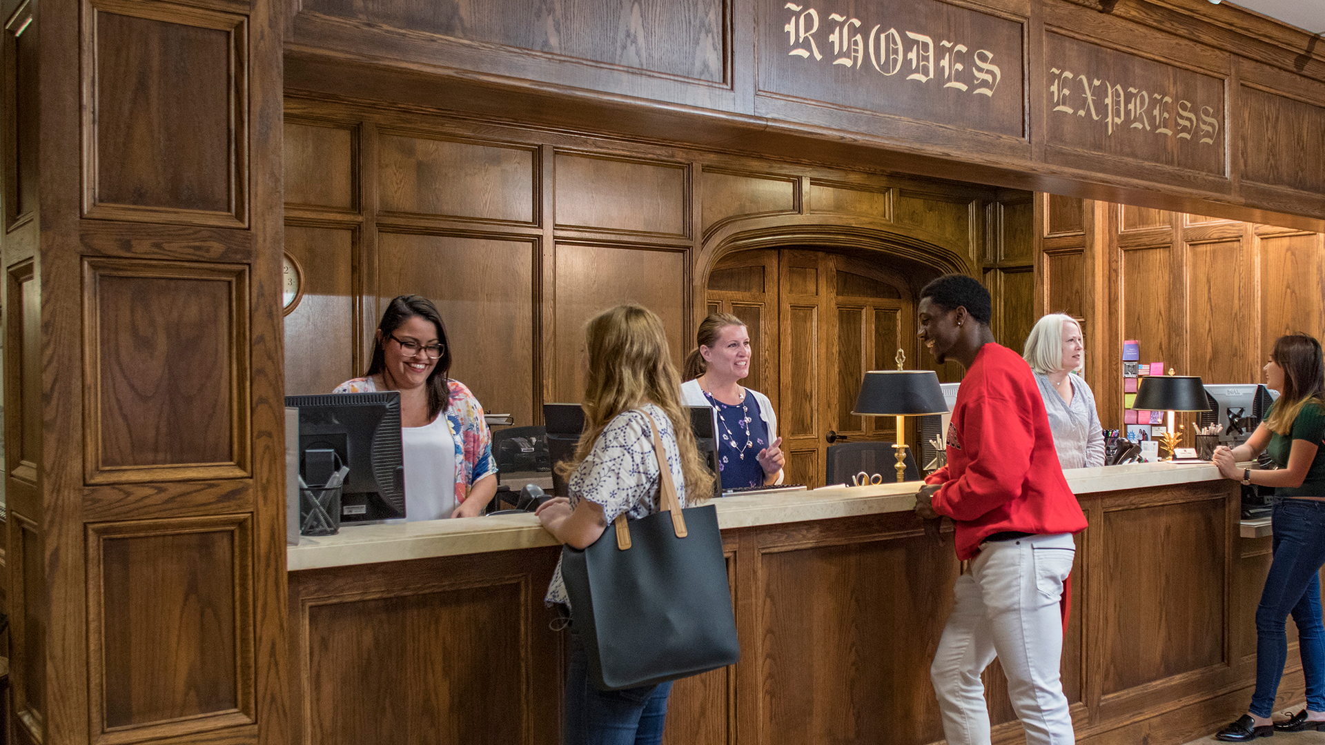 students doing business at a counter with oak paneling in the background.