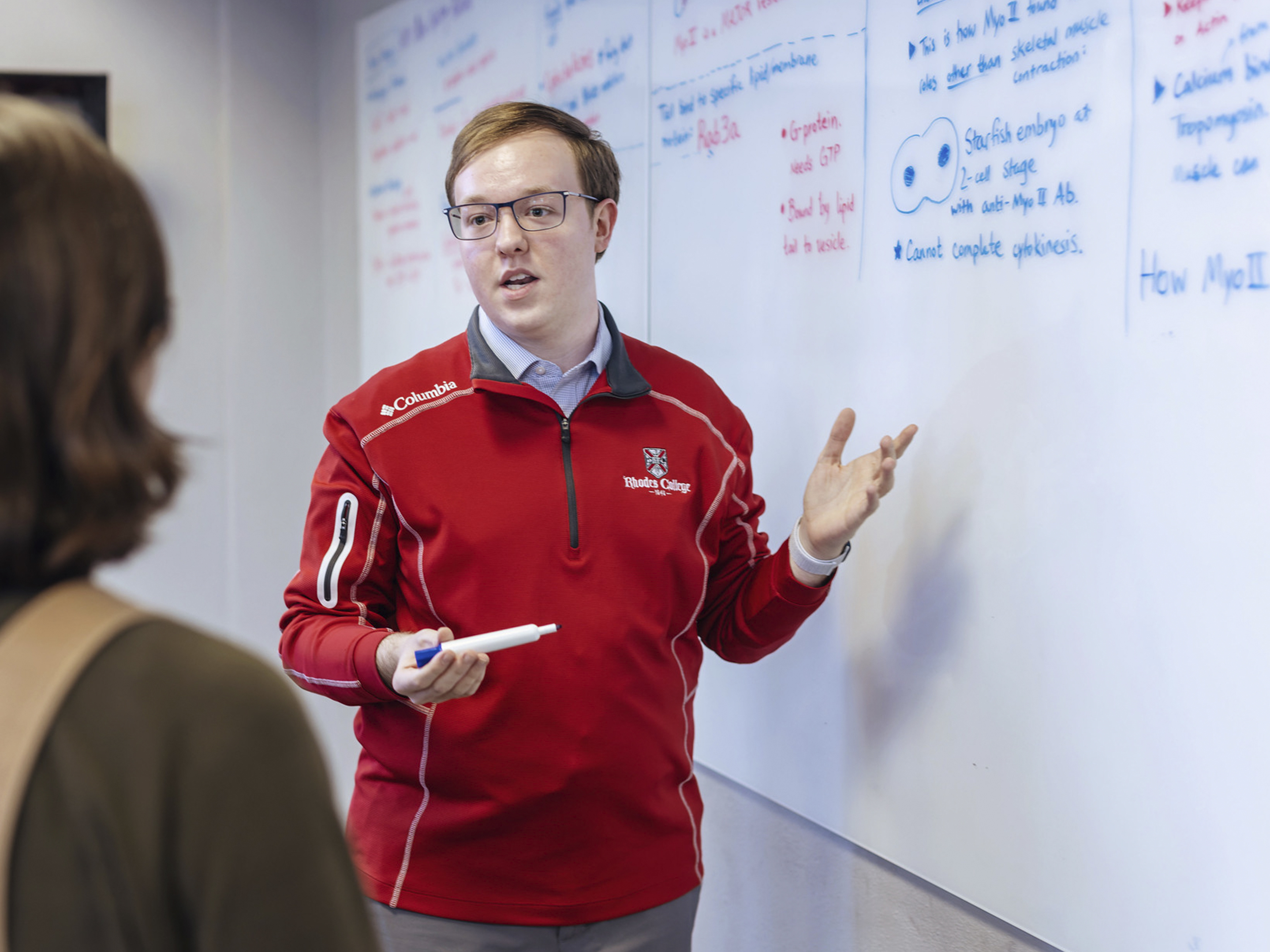 a young man gestures at a whiteboard