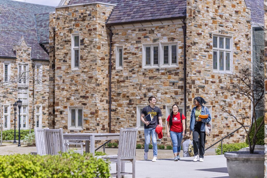 A group of three students on a spacious walkway with a two-story, collegiate gothic building in the background.