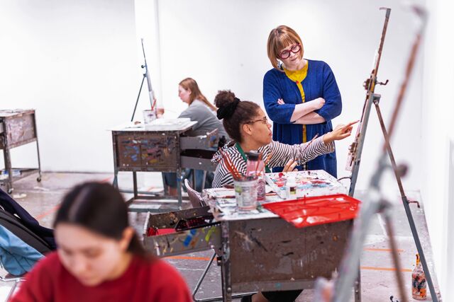 A professor and student discuss a painting in progress.
