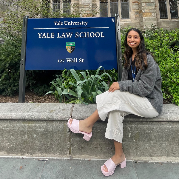 a yoiung woman with long dark hair in front of a sign that says Yal Law School