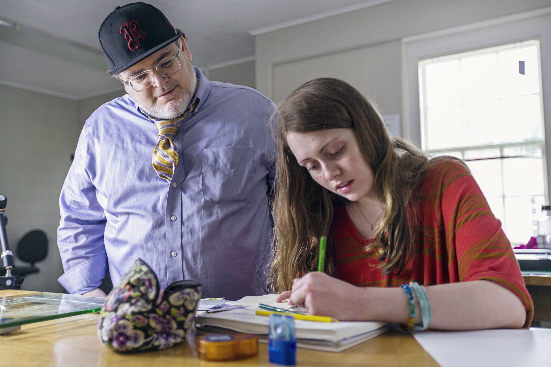 a professor looks on as a student writes on paper
