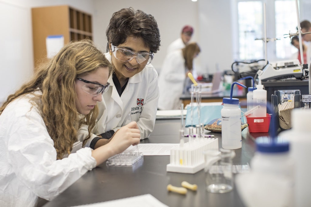A professor helps her student, who is examining her lab experiment.