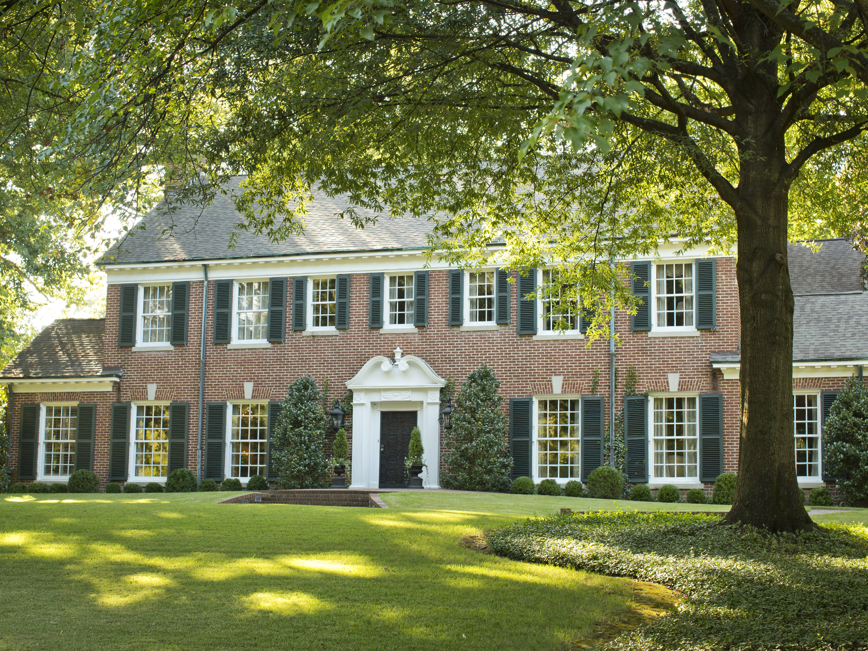 A red brick Georgian style home shaded by trees