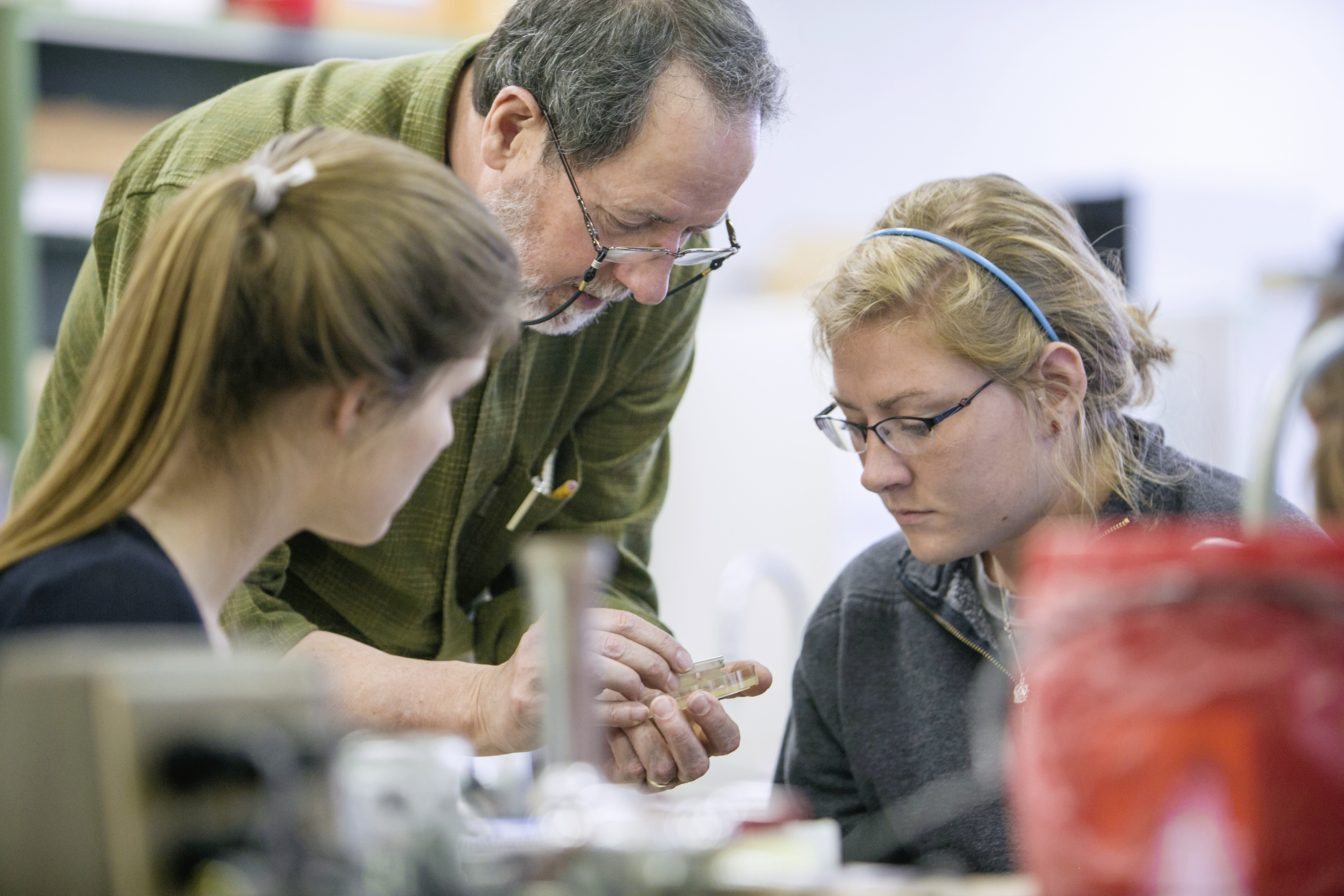 A professor bends over to show two students a science demonstration