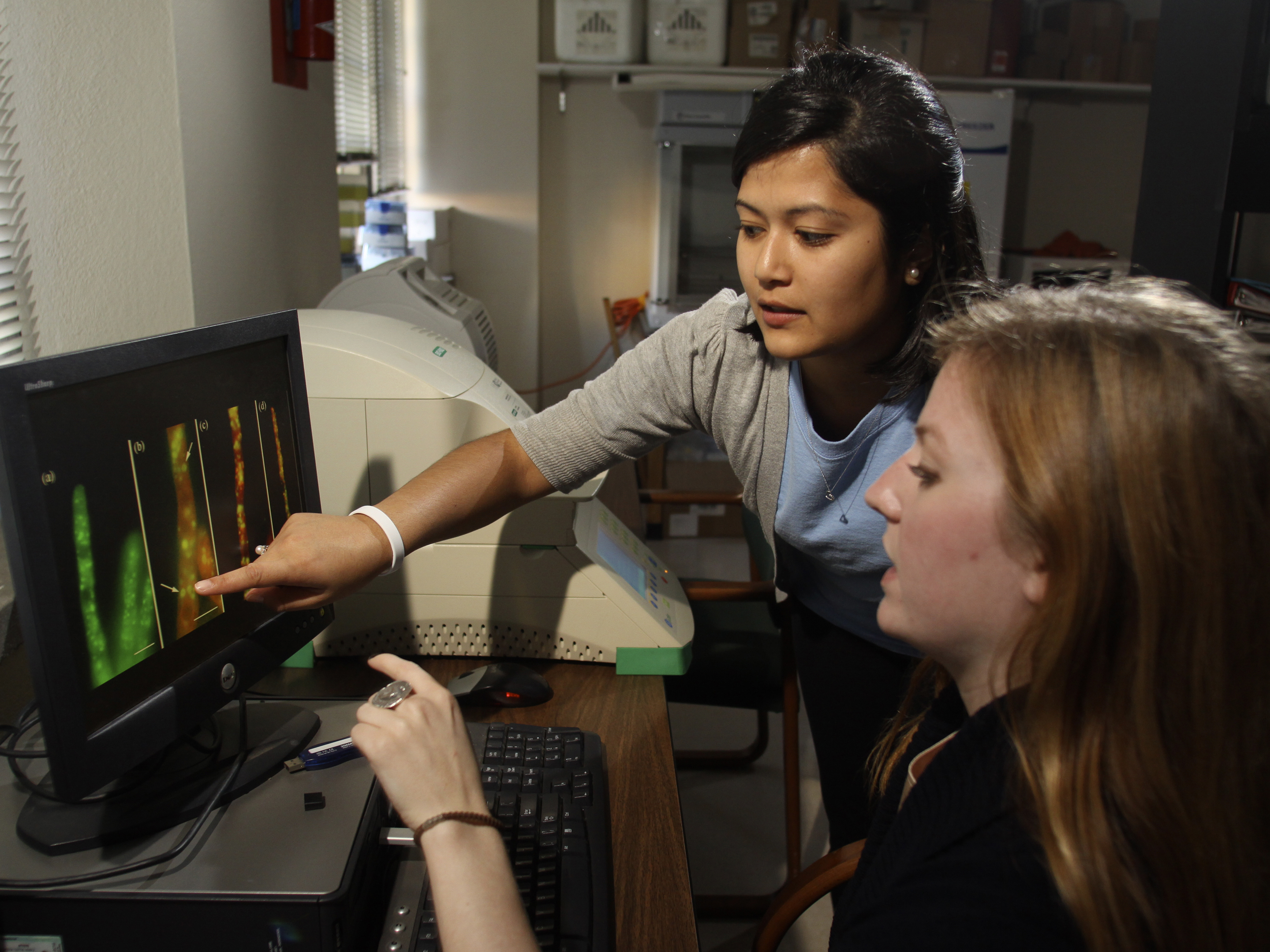 Two woman work at a computer. One points to something on the screen.