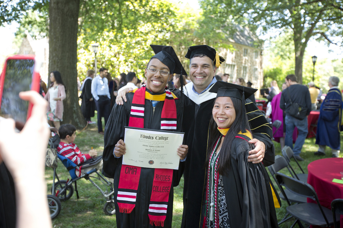 Students and a professor pose for a photo in graduation regalia