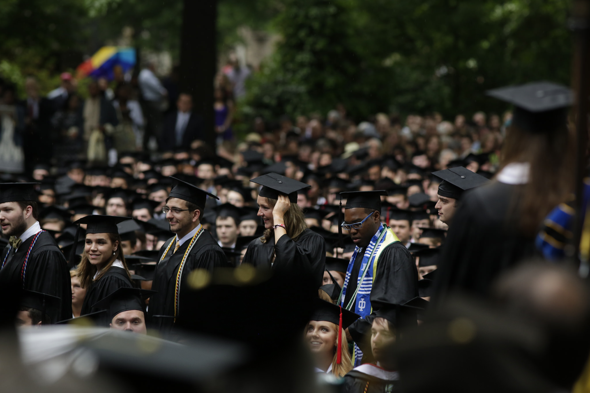 A procession of graduates in their caps and gowns make their way among the rows of seated graduates