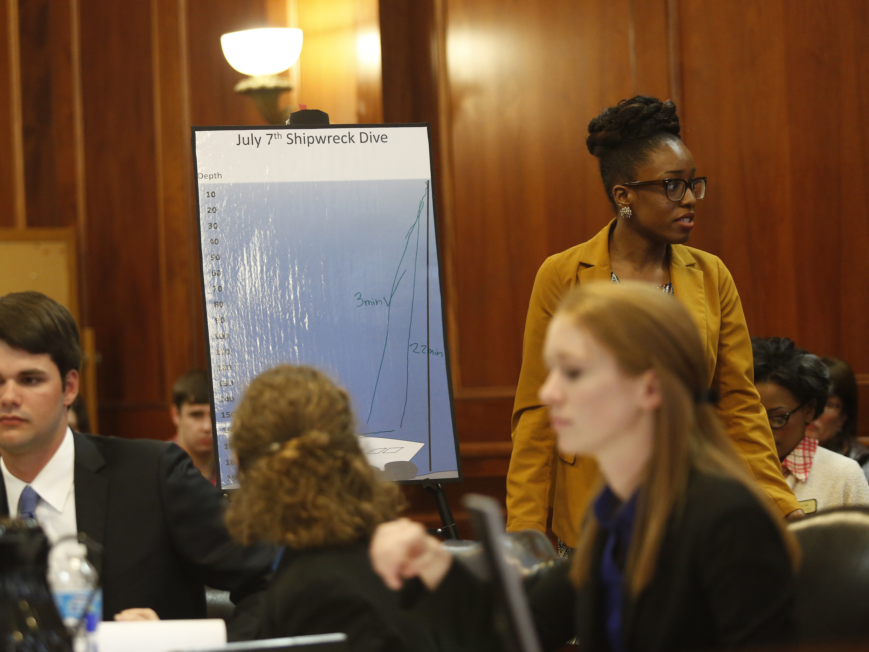 Students in suits sit and stand around an exhibit poster