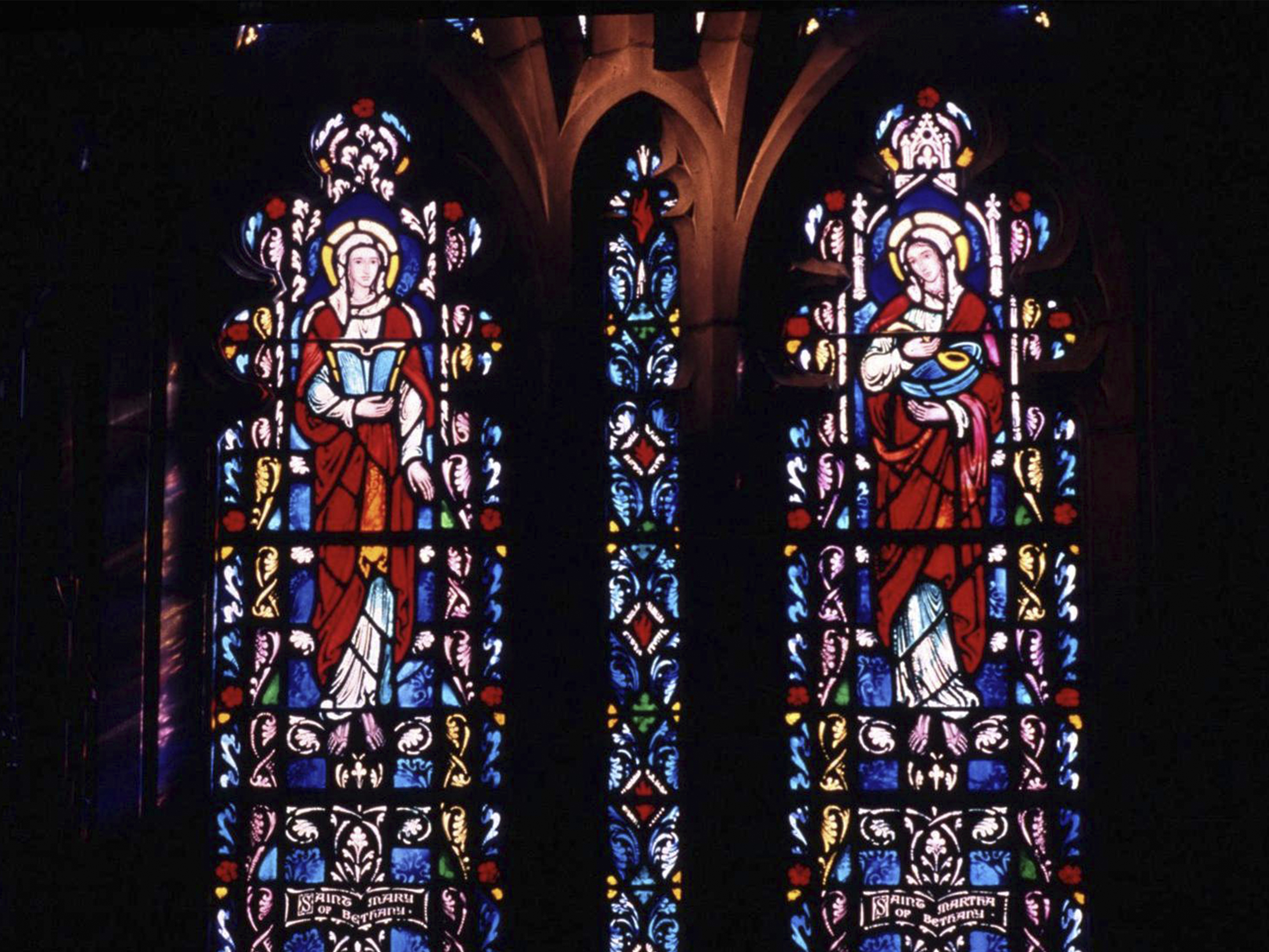 Two panels of stained glass featuring Mary Magdalene and Mary, mother of Jesus on a stone chapel wall