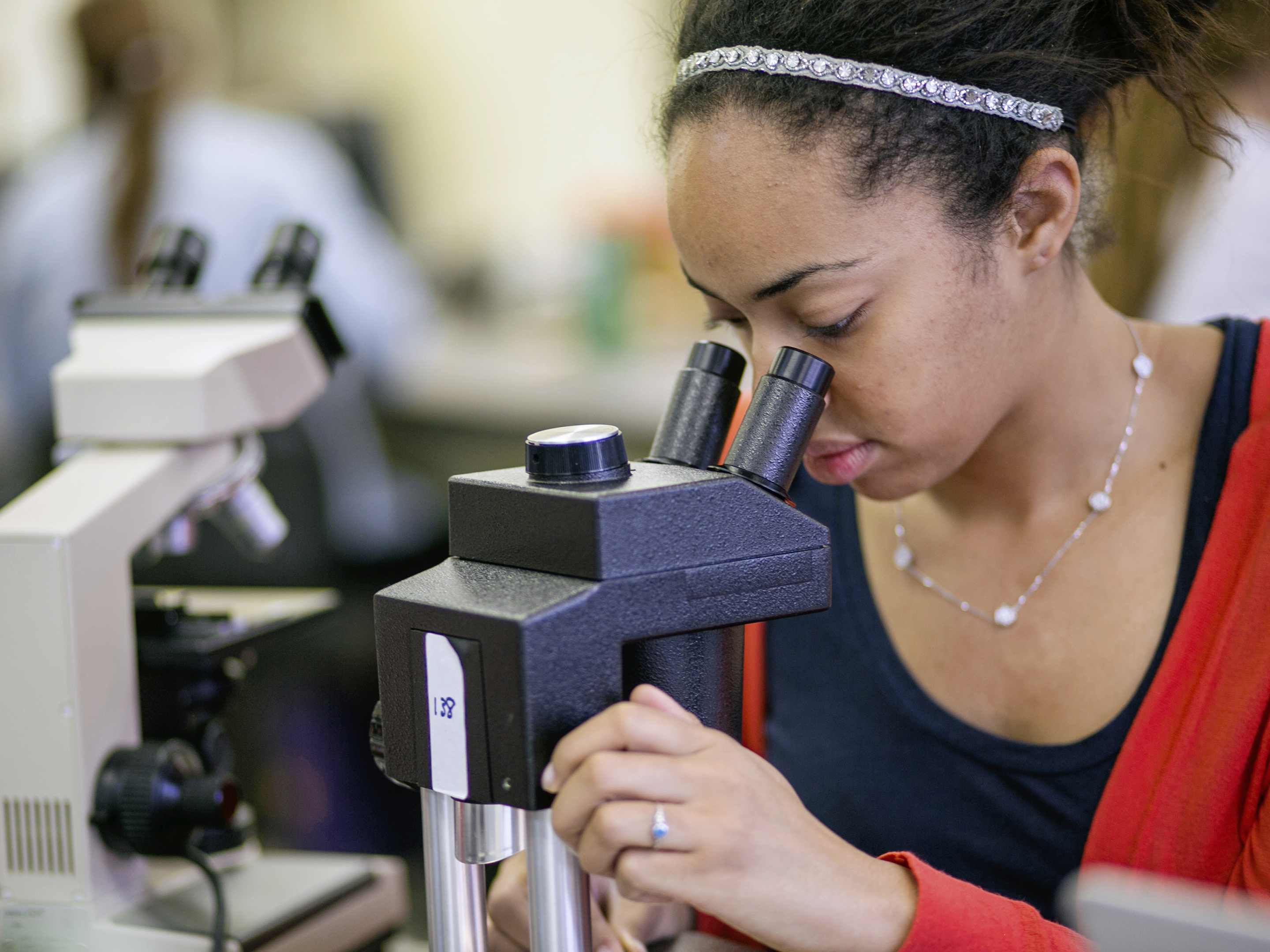 A young woman looks through a microscope.