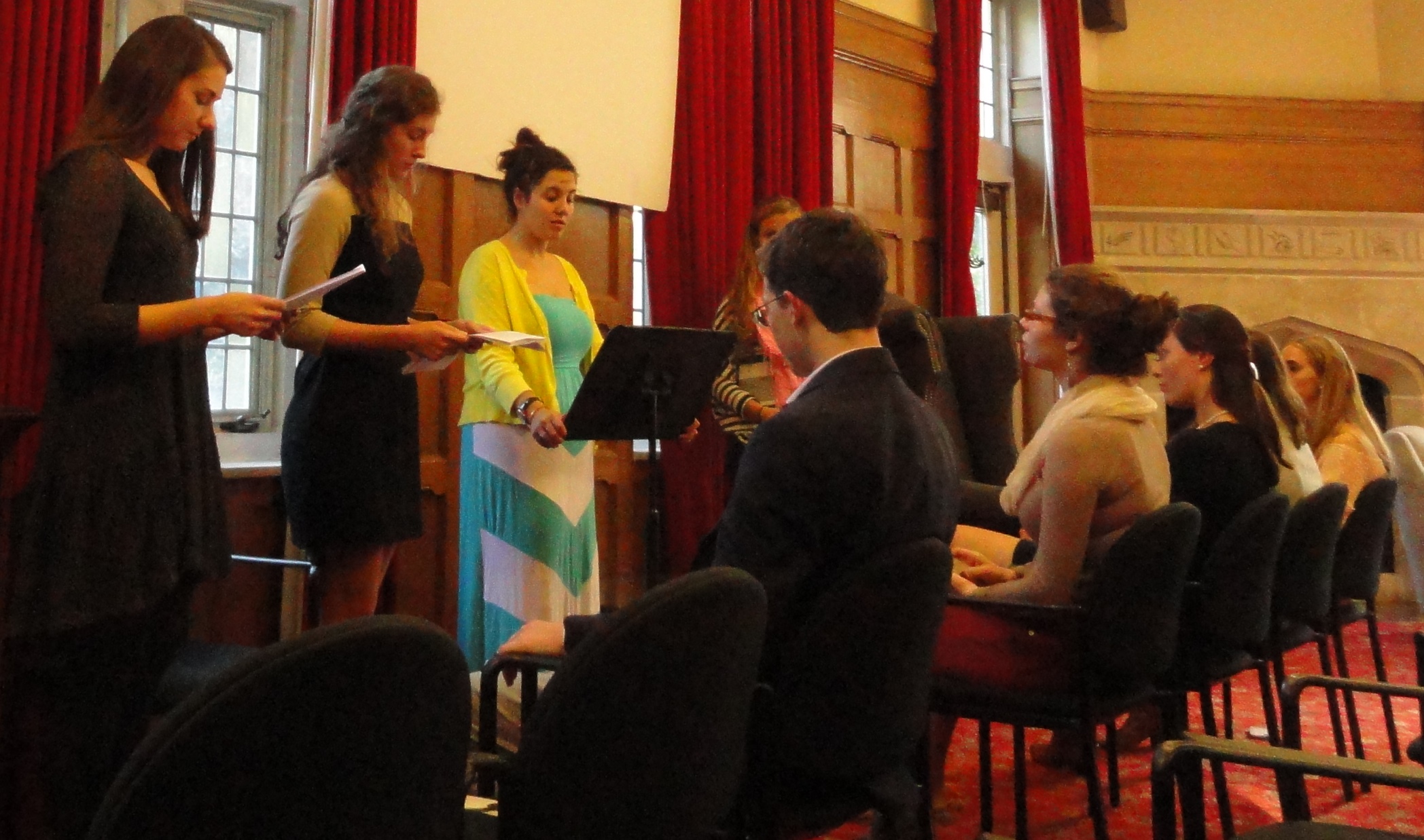 three female students on a stage in front of seated students