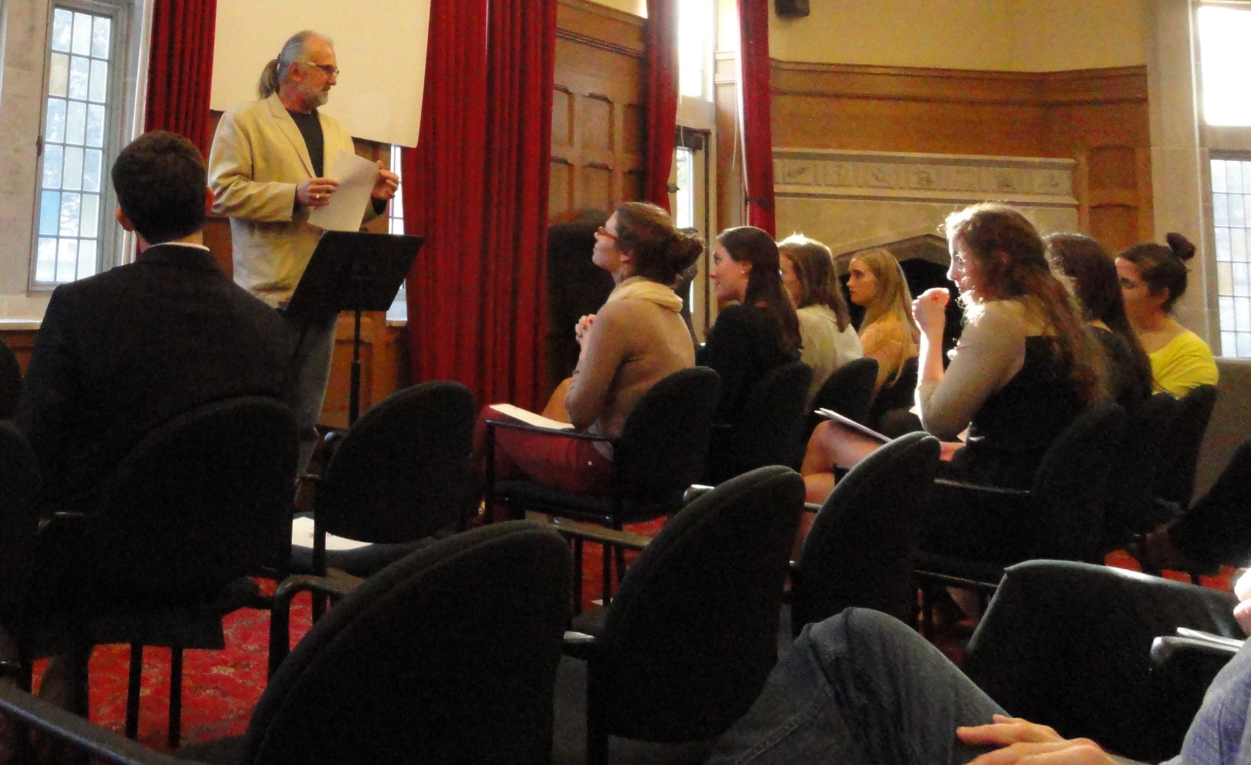 a male professor with gray hair in a ponytail gives a reading in front of students