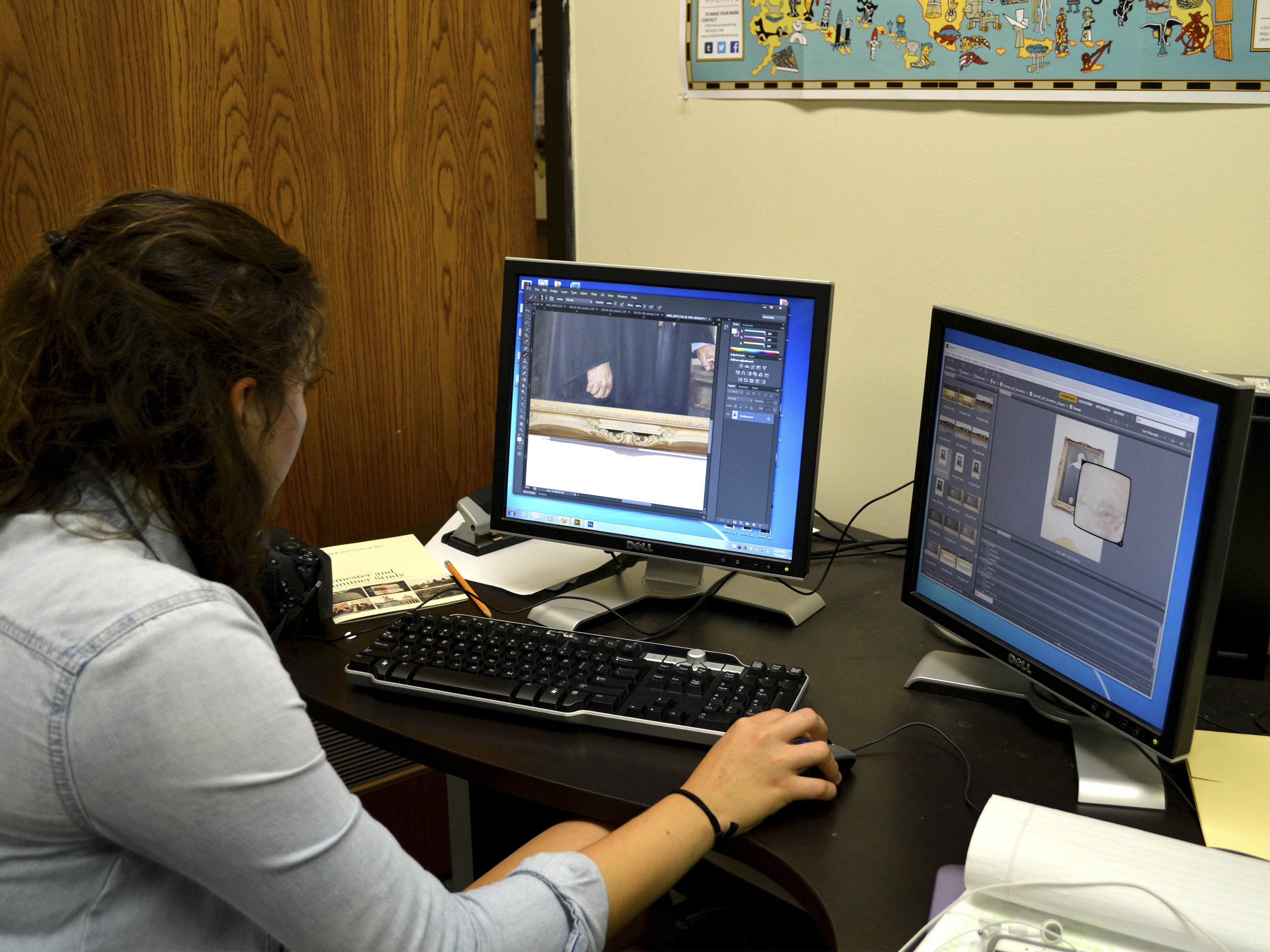 A dark haired young woman works at a computer with two screens