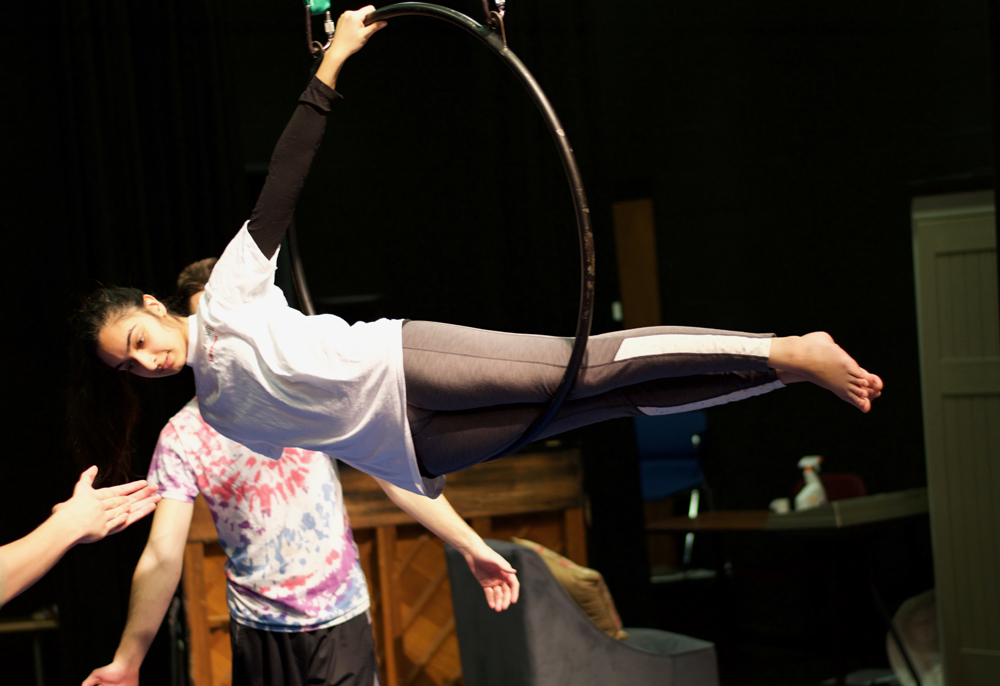 A female college student allowing a hanging metal hoop to support her lower body weight while she reaches back