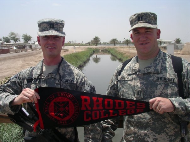 Two male students in US Army fatigues hold a Rhodes College Banner