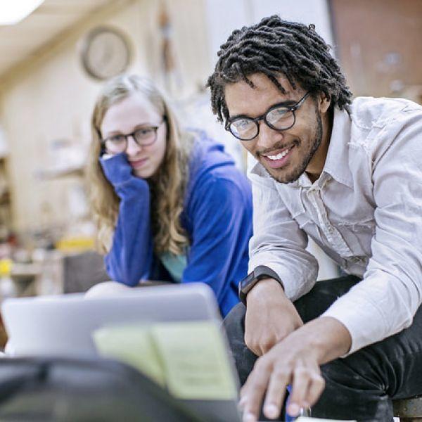 A young man and a young woman look together at a laptop.