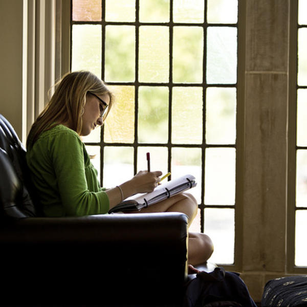 A student sits in an armchair in front of stained glass