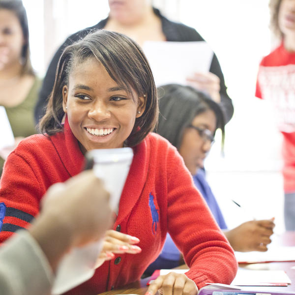 A young woman wearing a red sweater smiles and looks at a student off-camera