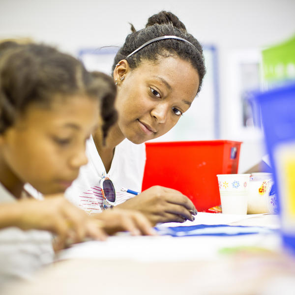 A young woman helps a girl with a task
