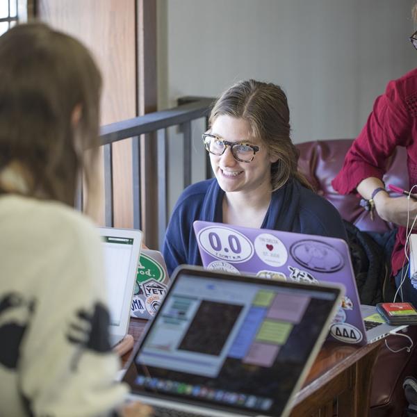 A group of people at a table discuss what is on their laptops.