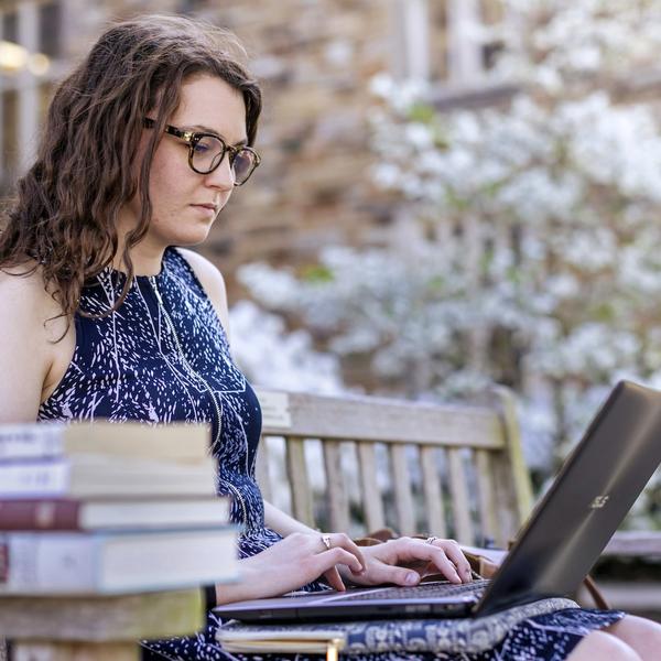 A young woman sits on a bench, looking at her laptop.
