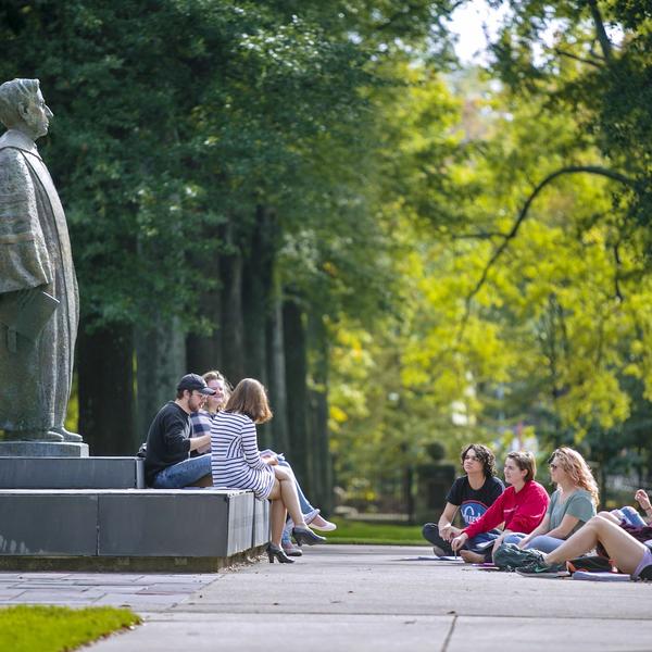 Students on a tour gather in front of a tall bronze statue of a man.