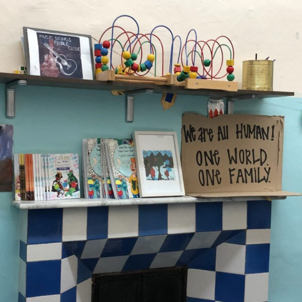 A shelf on a blue wall covered in books, toys, and a sign that reads: "We are all human. One world. One family."