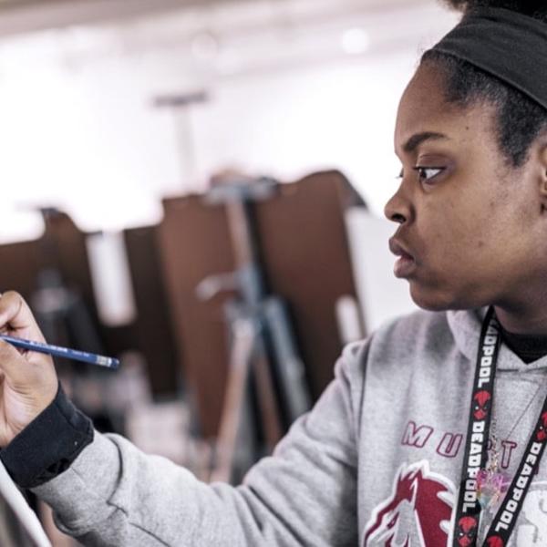 A student draws with her art board propped up on an easel. 