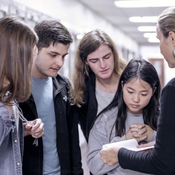 A group of young people on a scavenger hunt huddle around a young woman holding a map