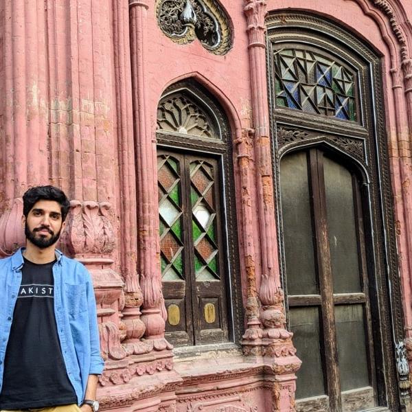 A young man stands casually beside a mosque.