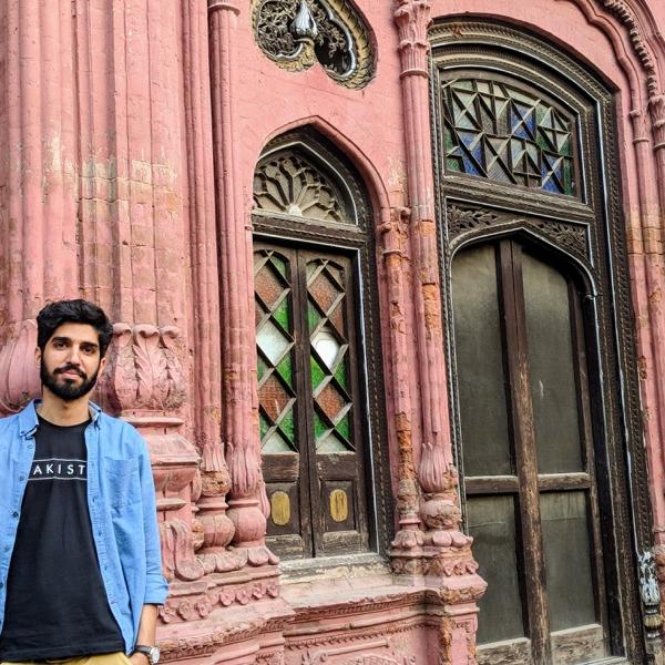 A young man in a blue shirt leans against a mosque.