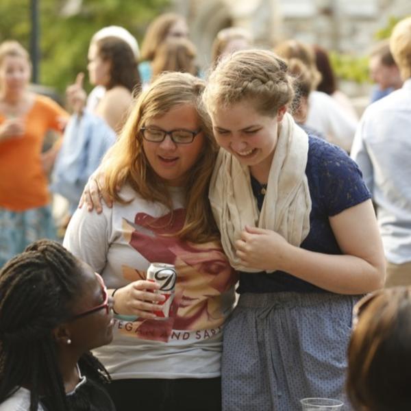 Two friends laugh and embrace as they meet at a picnic