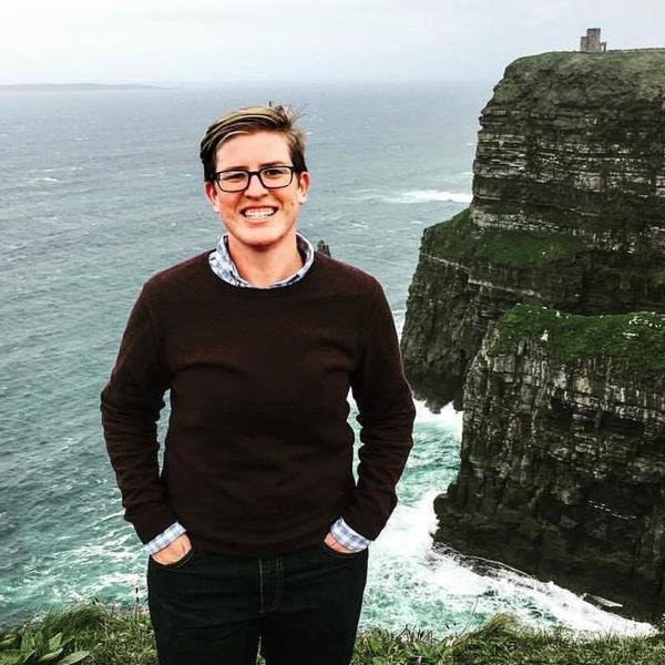 A woman with short hair stands on a cliff in front of the sea