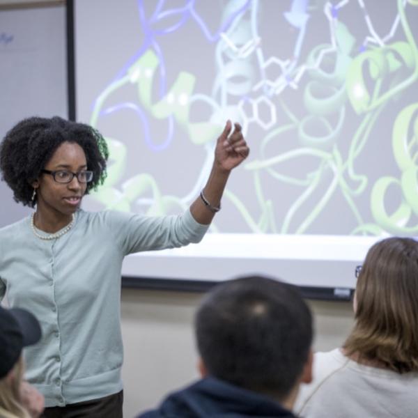 A professor pointing at a whiteboard behind her.