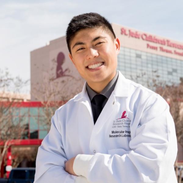 A young man in a lab coat stands in front of St Jude Children's Research Hospital.