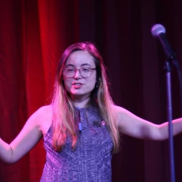 A young woman on stage in front of a red curtain.