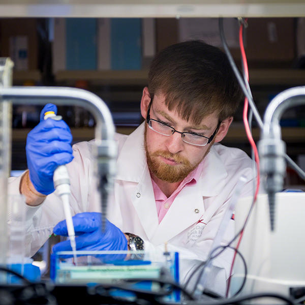 student in a lab coat measures a liquid into a pipettte