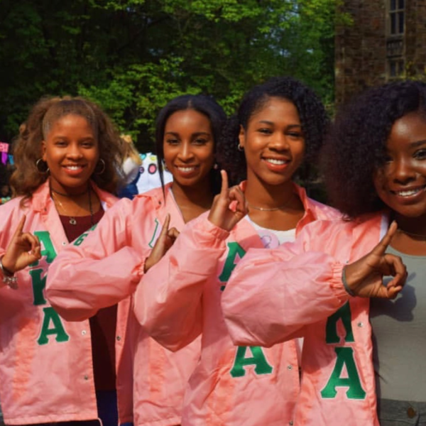 Four women in pink jackets holding up AKA letters