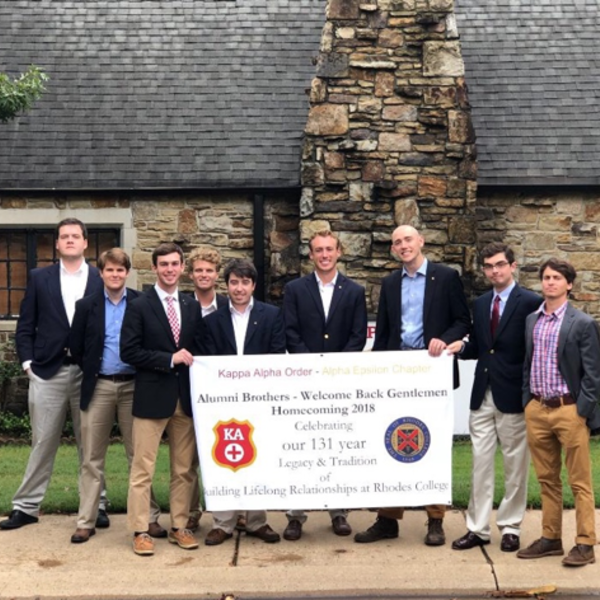 Men standing in front of stone house with banner