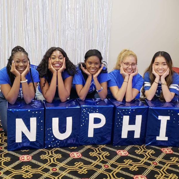 Five women wearing blue shirts and posing on top of blocks that read "nu phi"