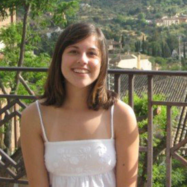 a young woman with shoulder-length hair sits on a bench with a mountainous background