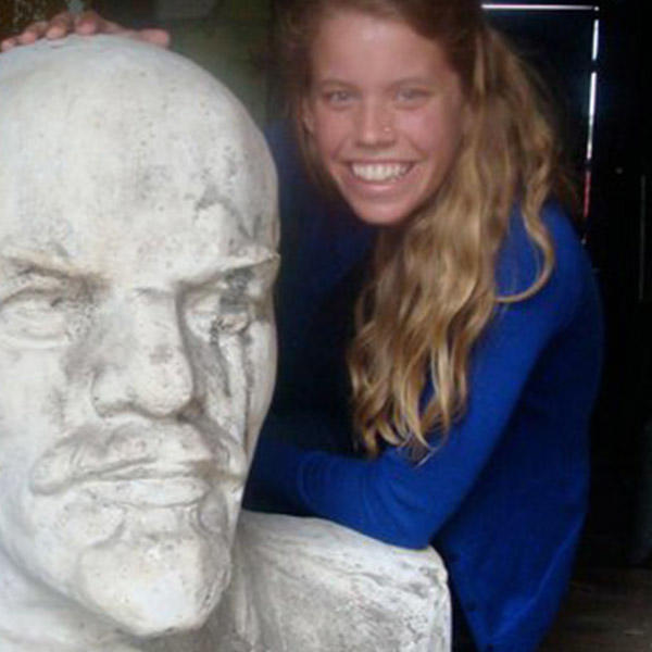 a female with long blonde hair sits next to large sculpture