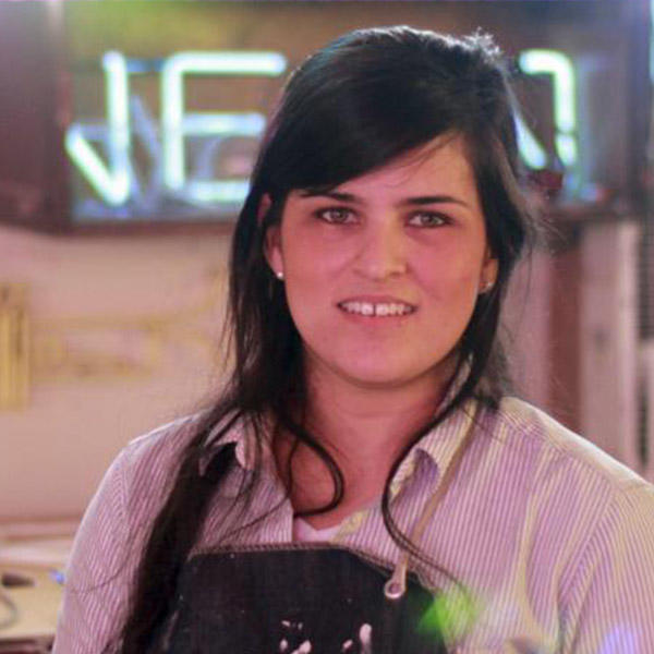 a young woman with dark hair with a neon sign in the background