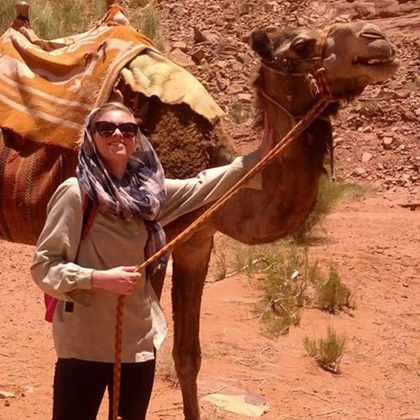 a young woman in a head scarf holds the reins to a camel