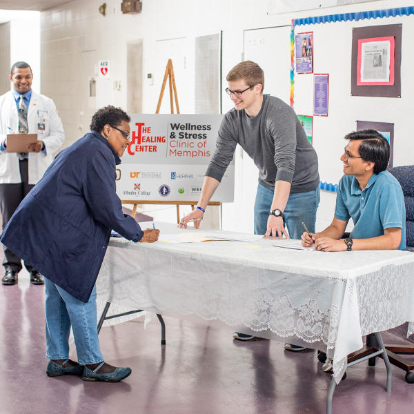 two students help a woman sign up at a health clinic